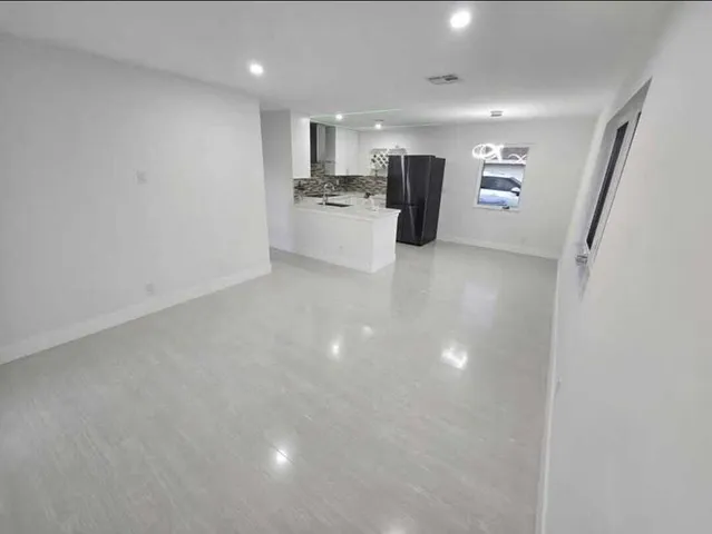 a view of a room with a refrigerator wooden floor and windows