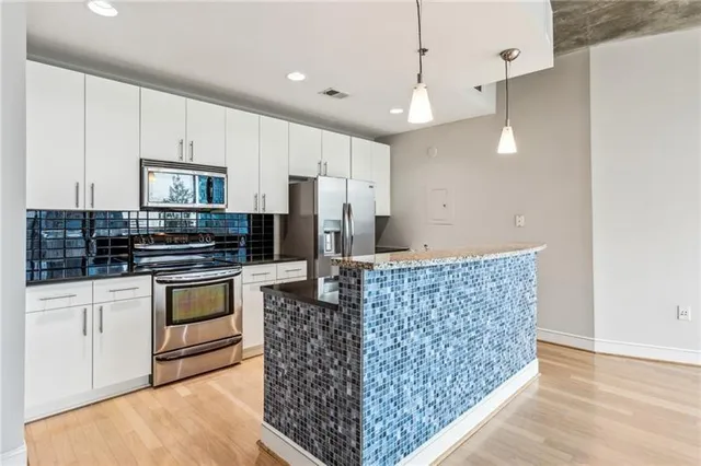 a kitchen with stainless steel appliances kitchen island granite countertop a stove a sink dishwasher a refrigerator and white cabinets with wooden floor