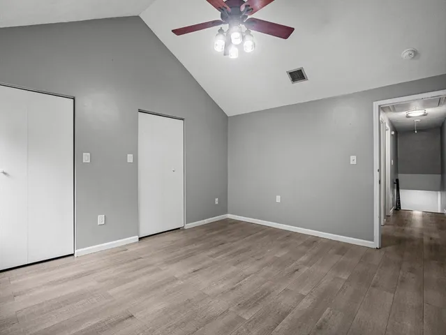 an empty room with wooden floor chandelier fan and windows