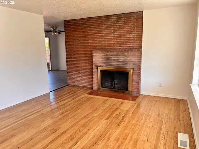 a view of an empty room with wooden floor and a fireplace