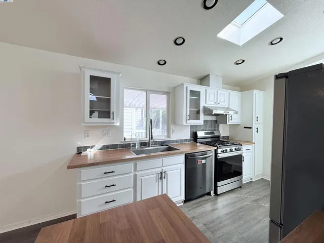 a kitchen with stainless steel appliances a stove a sink dishwasher a refrigerator and white cabinets with wooden floor