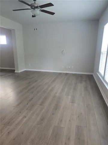 an empty room with wooden floor fan and windows