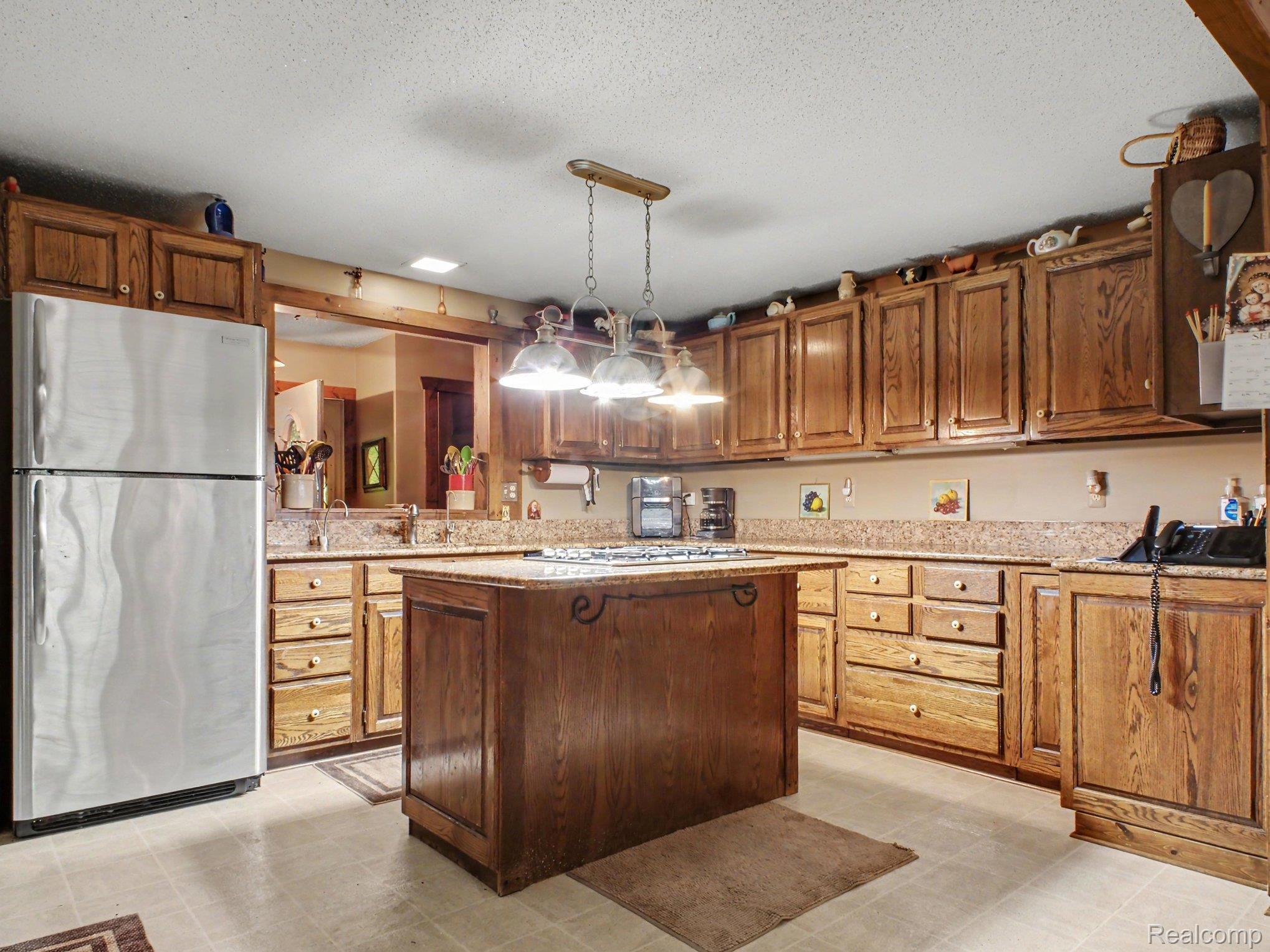 3284 Pratt Road Metamora, MI 48455 - Photo 7 of 22 Kitchen featuring wood cabinetry, a center island with a cooktop, granite-style countertops, stainless steel refrigerator, and recessed lighting