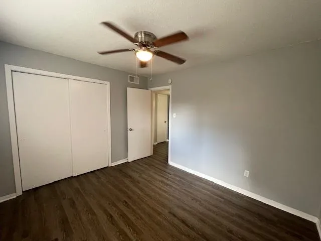 an empty room with wooden floor fan and windows
