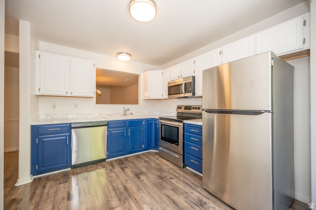 1799 West 1110th Street North Provo, UT 84604 - Photo 9 of 24 Kitchen featuring wood-finish flooring, two-tone cabinetry with white upper and blue lower units, stainless steel appliances, and a pass-through window