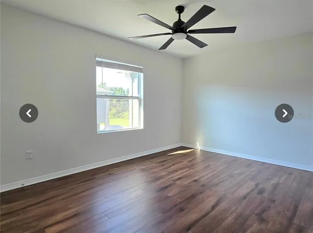 an empty room with wooden floor ceiling fan and windows