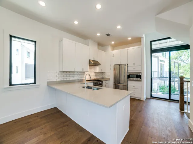 a kitchen with stainless steel appliances a stove top oven a sink a refrigerator a center island and a hard wood floor