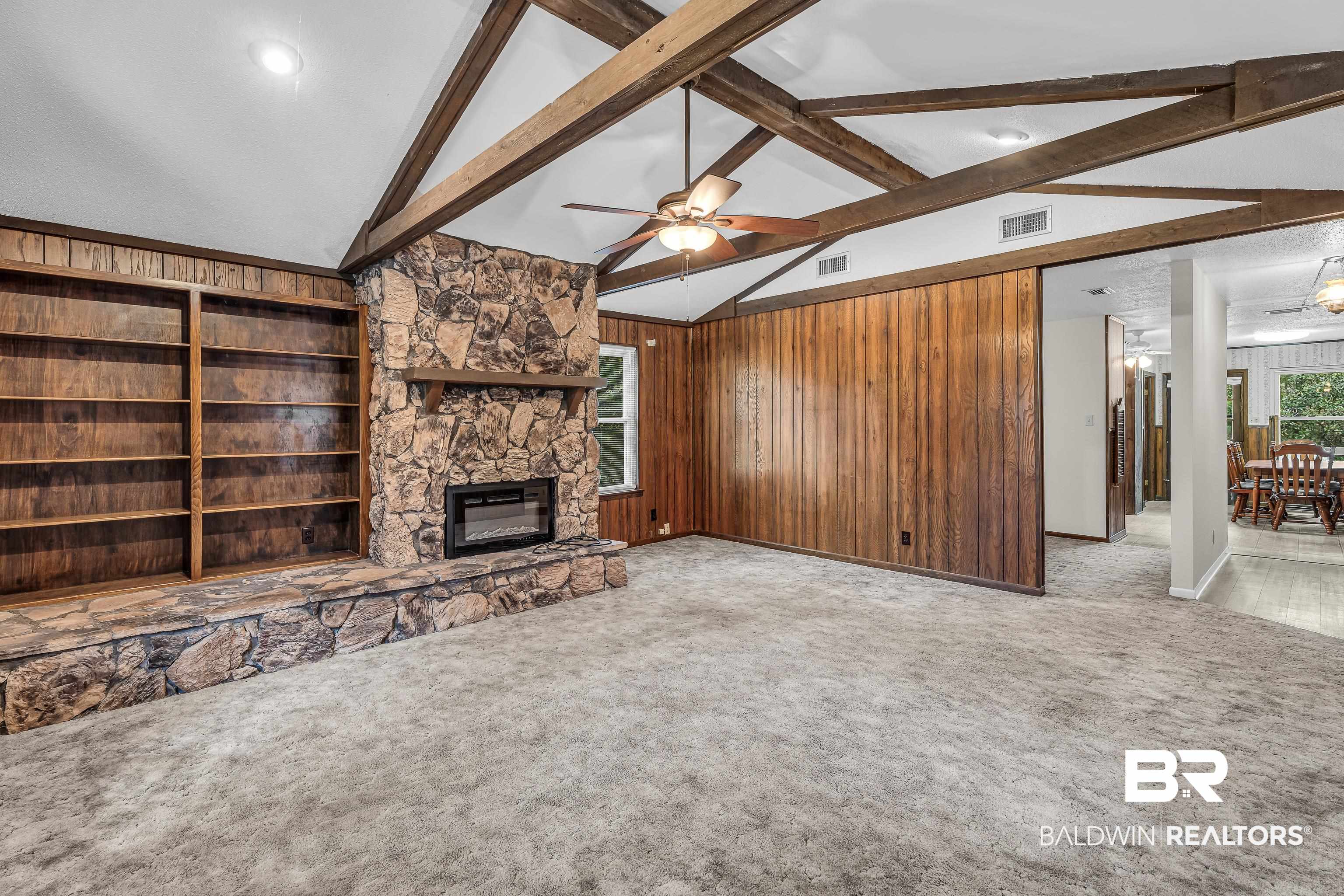 22970 River Road South Daphne, AL 36526 - Photo 29 of 48 Unfurnished living room with wood walls, carpet, a ceiling fan, and a stone fireplace