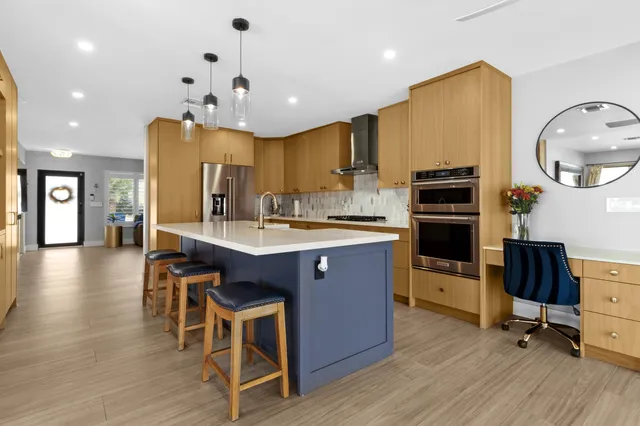 a kitchen with stainless steel appliances kitchen island granite countertop a stove a sink a refrigerator and chairs with wooden floor