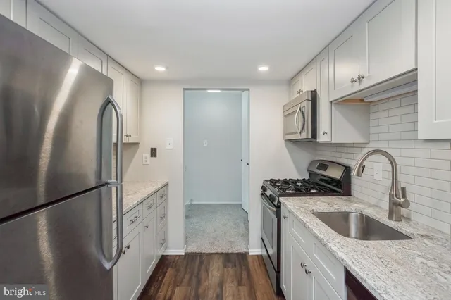 a kitchen with stainless steel appliances granite countertop a refrigerator a sink a stove and a refrigerator with wooden floor