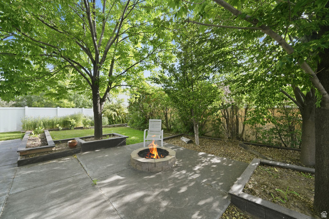 1464 990 West Provo, UT 84601 - Photo 37 of 41 Expansive backyard featuring a concrete patio, a stone-finish fire pit, raised garden beds, mature trees, and a white privacy fence
