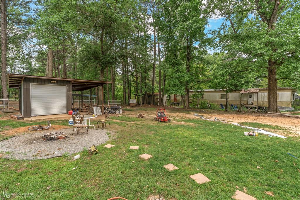 143 New Bethel Booker Road Benton, LA 71006 - Photo 15 of 26 Expansive grassy yard with mature trees, featuring a detached metal-sided structure with an overhead door and a covered overhang