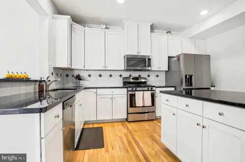 a kitchen with stainless steel appliances white cabinets a sink a stove a refrigerator and cabinets