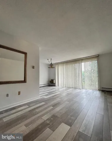 a view of an empty room with wooden floor and fan