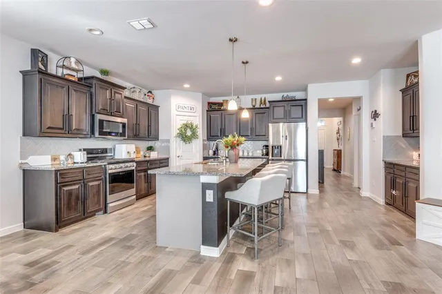 a kitchen with stainless steel appliances kitchen island granite countertop a stove top oven a sink dishwasher a refrigerator and a dining table with wooden floor