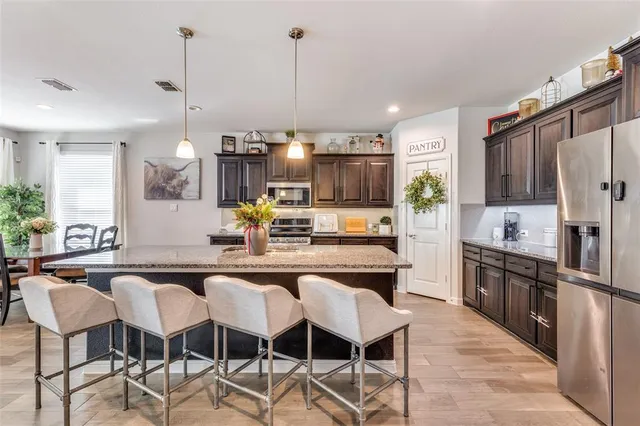a kitchen with stainless steel appliances kitchen island granite countertop a table chairs and a refrigerator