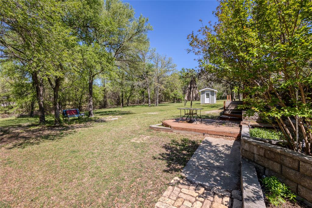 1701 Central Road Weatherford, TX 76088 - Photo 32 of 40 View of green lawn featuring a wooden deck, a storage shed, and view of wooded area