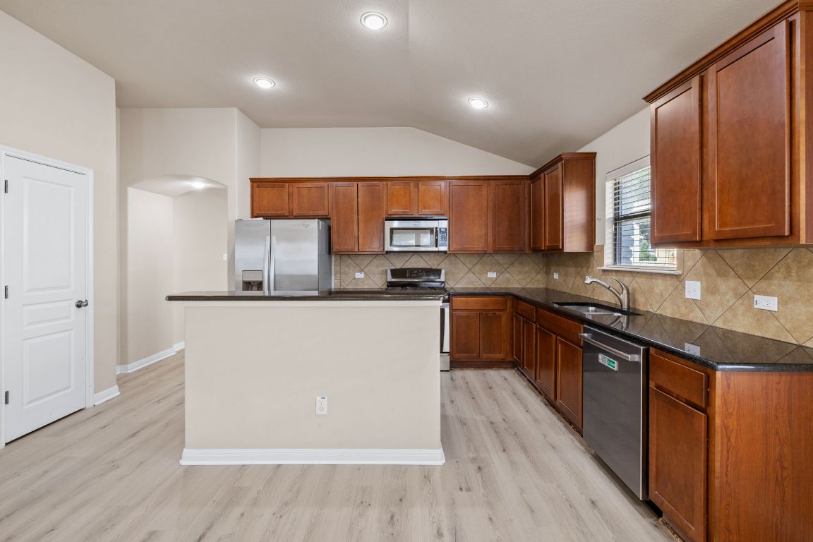 1900 Main Street Cedar Park, TX 78613 - Photo 11 of 34 a kitchen with granite countertop wooden cabinets a sink and a stove with wooden floor