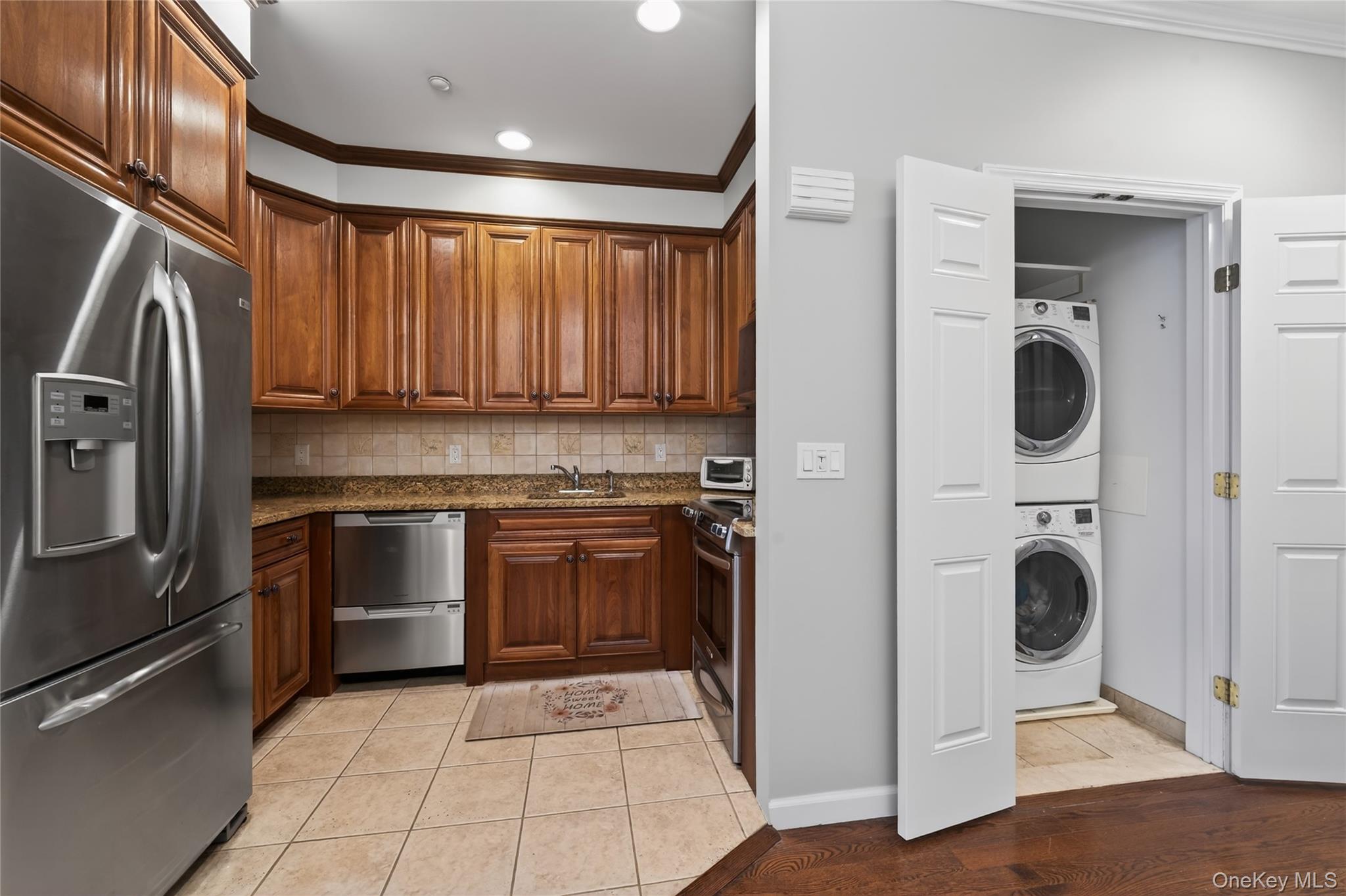 294 Spring Drive East Meadow, NY 11554 - Photo 11 of 31 Kitchen featuring ornamental molding, appliances with stainless steel finishes, dark stone counters, stacked washer and clothes dryer, and light tile patterned flooring