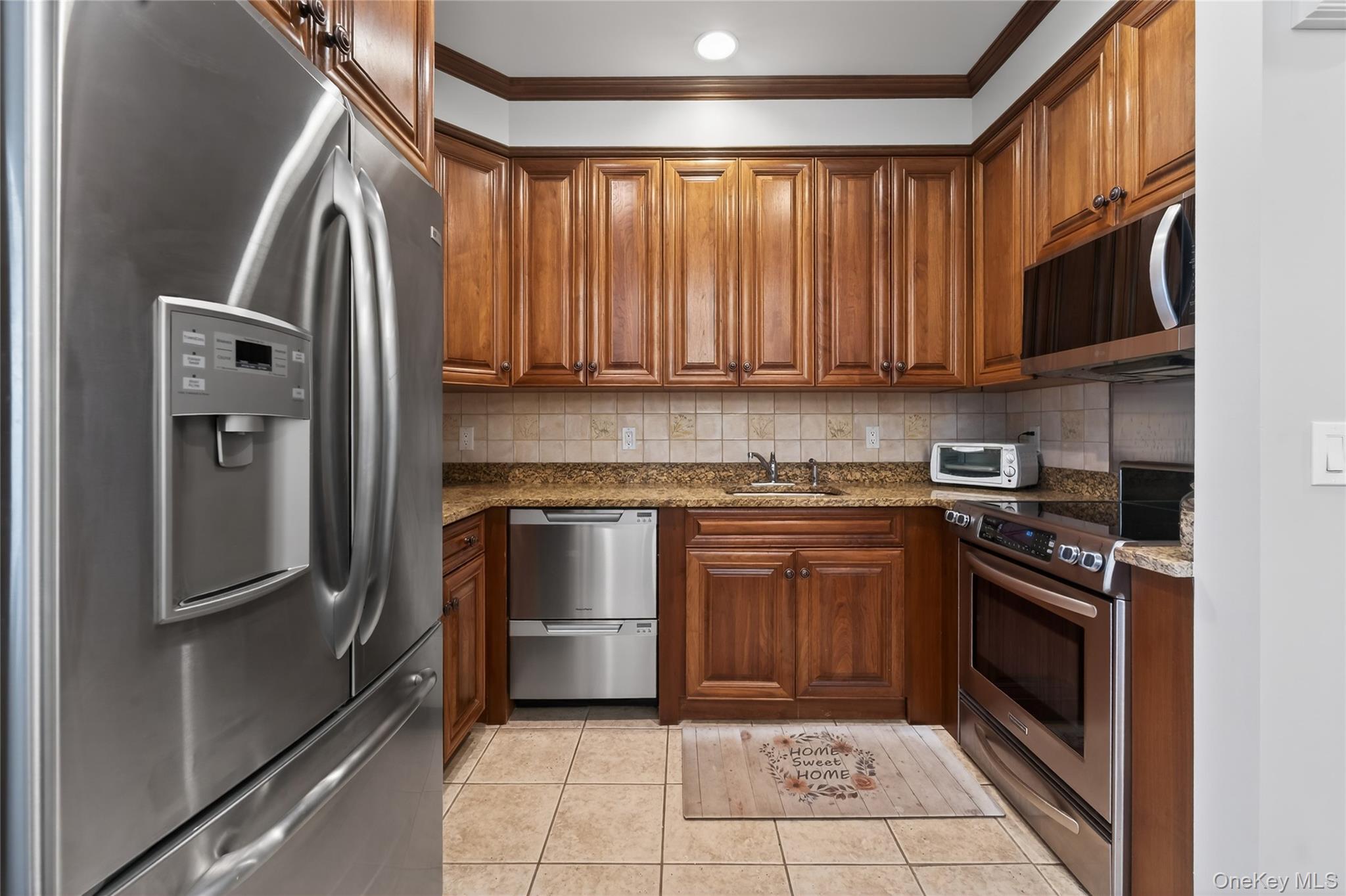 294 Spring Drive East Meadow, NY 11554 - Photo 8 of 31 Kitchen with stainless steel appliances, dark stone countertops, ornamental molding, brown cabinetry, and light tile patterned flooring