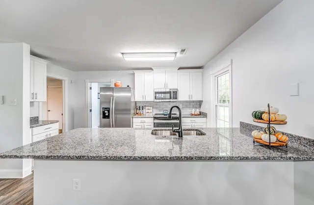 a kitchen with stainless steel appliances granite countertop a sink dishwasher a stove a dining table and chairs with wooden floor