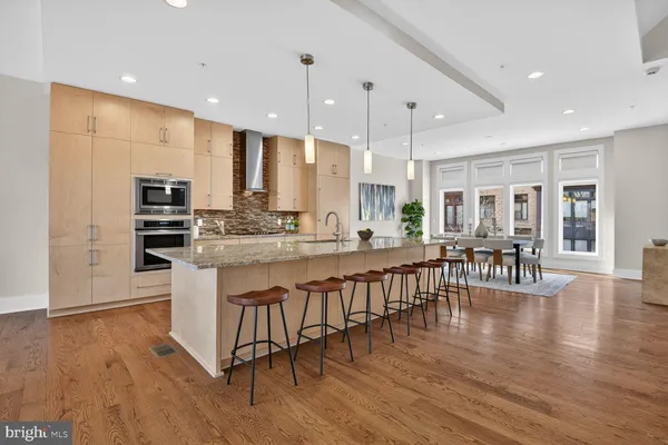 a kitchen with stainless steel appliances granite countertop a stove top oven a sink a dining table and chairs with wooden floor