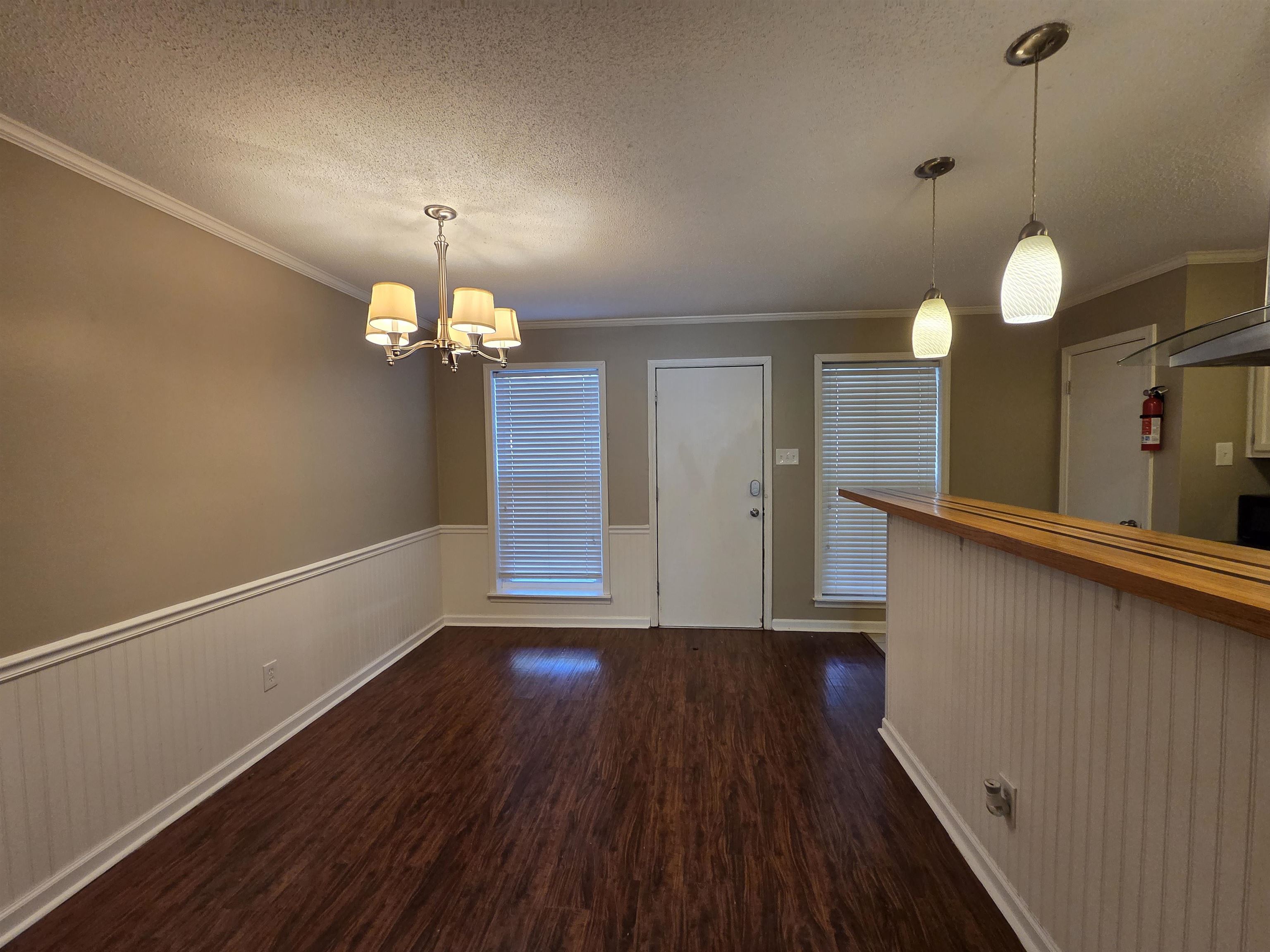 2104 Harbert Avenue Memphis, TN 38104 - Photo 5 of 26 Unfurnished dining area featuring a textured ceiling, a wainscoted wall, dark wood-style flooring, crown molding, and hanging lights