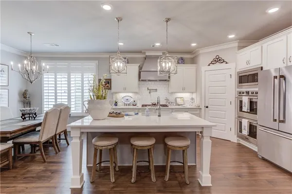 a kitchen with stainless steel appliances kitchen island granite countertop a dining table chairs and white cabinets