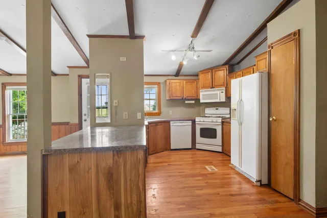 a kitchen with stainless steel appliances granite countertop a refrigerator a sink dishwasher a stove and white countertops with wooden floor