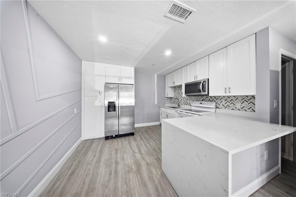 4375 Golden Gate Parkway Naples, FL 34116 - Photo 9 of 34 Kitchen featuring stainless steel appliances, white cabinets, a peninsula, light stone counters, and light wood finished floors