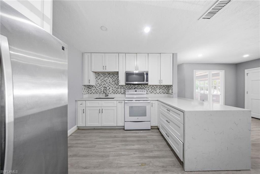 4375 Golden Gate Parkway Naples, FL 34116 - Photo 10 of 34 Kitchen with stainless steel appliances, white cabinets, a peninsula, light wood-style floors, and recessed lighting