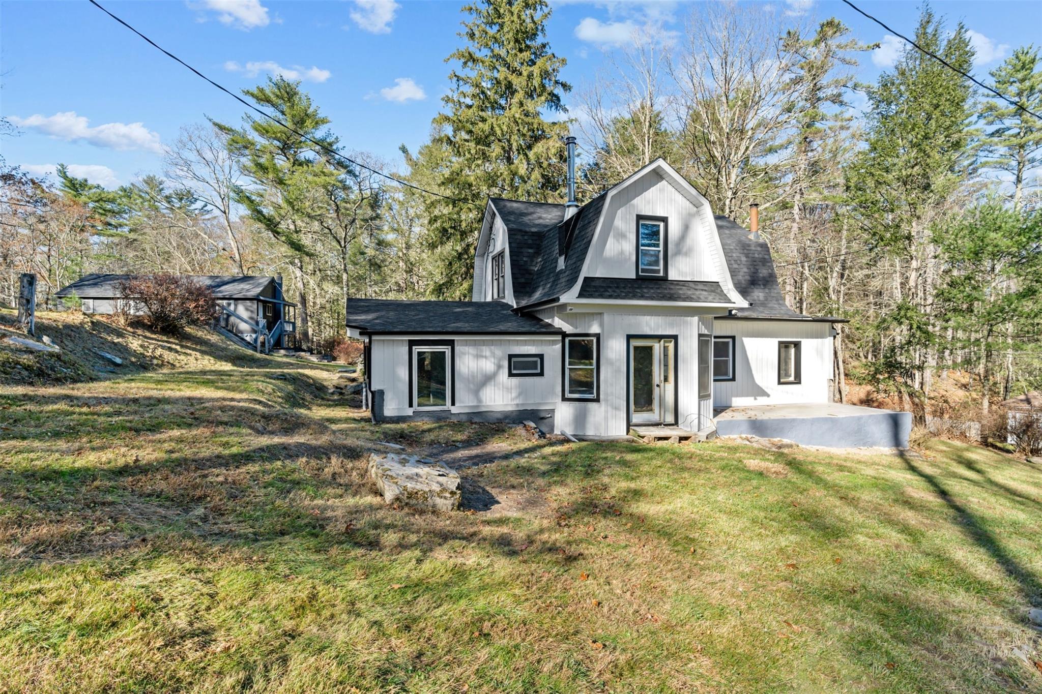 Rear view of property featuring a gambrel roof, a patio area, roof with shingles, and a lawn