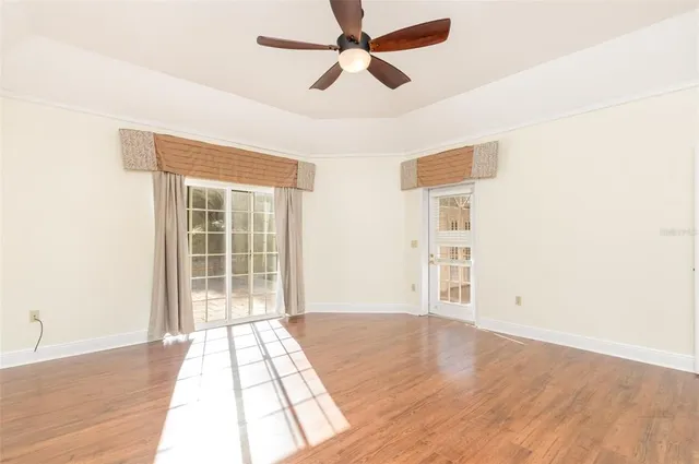 an empty room with wooden floor chandelier fan and windows