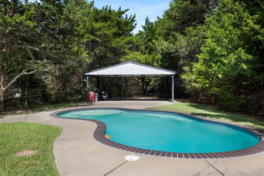401 Rugged Drive Red Oak, TX 75154 - Photo 33 of 40 Curved swimming pool with concrete decking, brick coping, and a detached metal carport structure