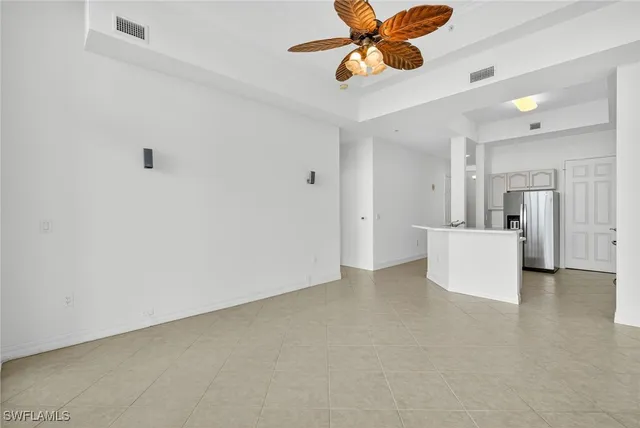a view of an empty room with a ceiling fan and kitchen view