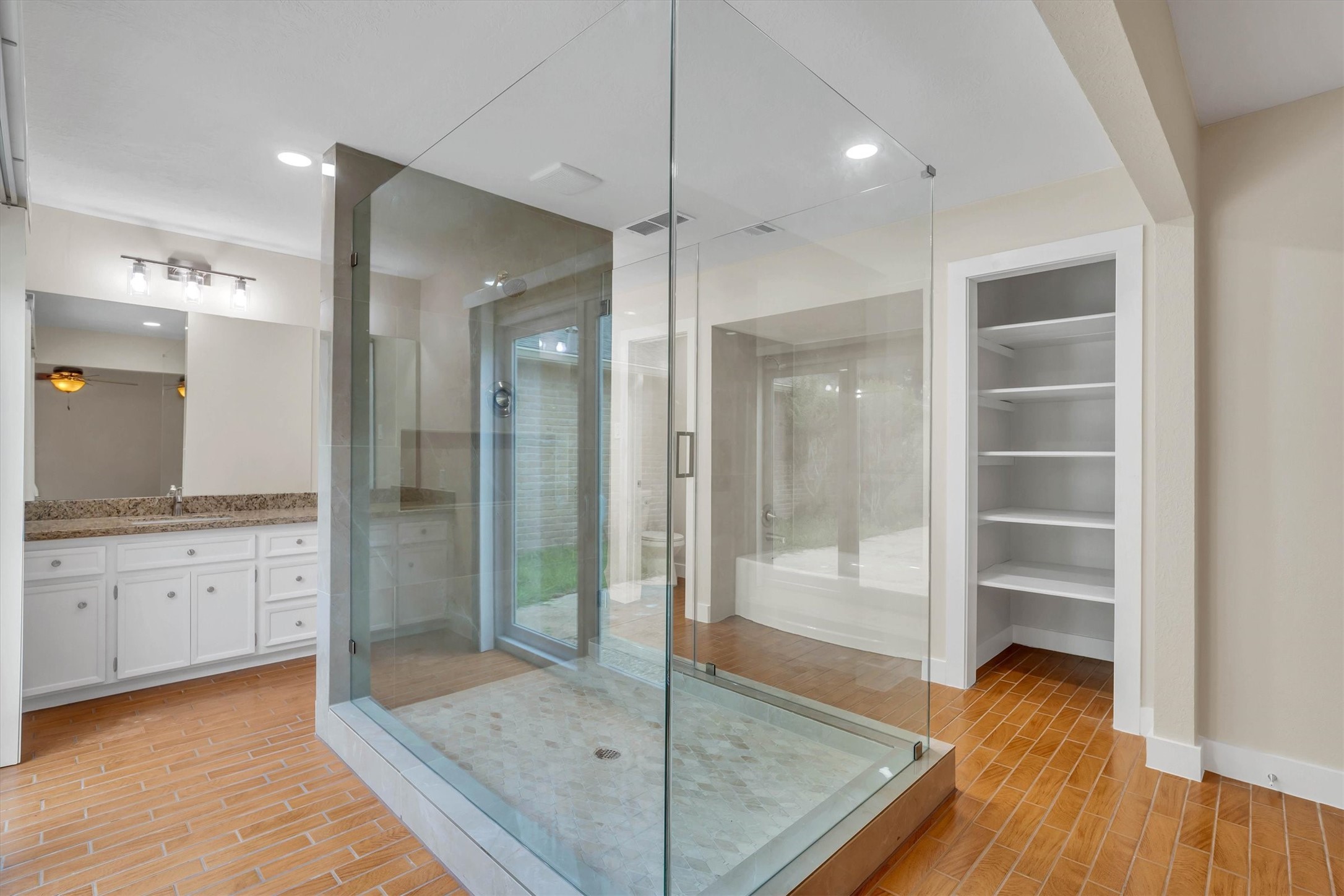 2163 Paso Rello Drive Houston, TX 77077 - Photo 35 of 45 This modern bathroom features a spacious glass-enclosed shower, a double-sink vanity with granite countertops, and built-in shelving for storage. The wood-look tile flooring adds warmth to the space.