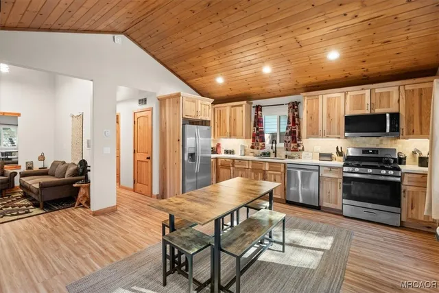 a kitchen with stainless steel appliances granite countertop a stove top oven a sink dishwasher a dining table and chairs with wooden floor