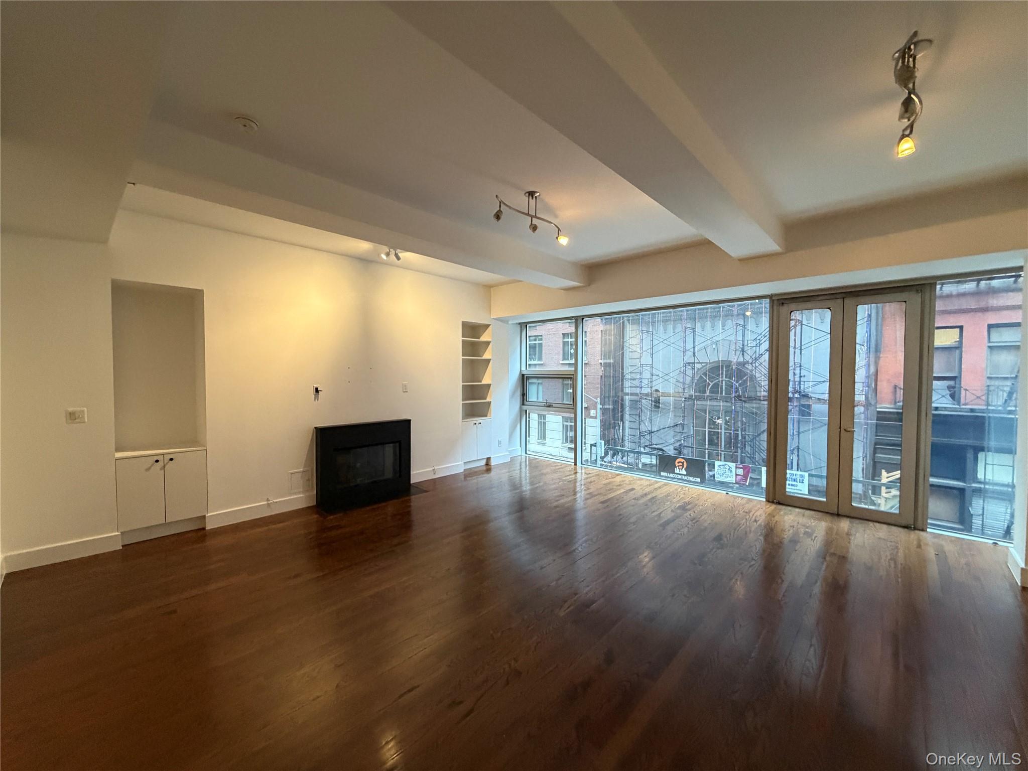 116 West 22nd Street, Unit 3 Manhattan, NY 10011 - Photo 2 of 11 Unfurnished living room featuring track lighting, beamed ceiling, dark wood-style flooring, and a fireplace