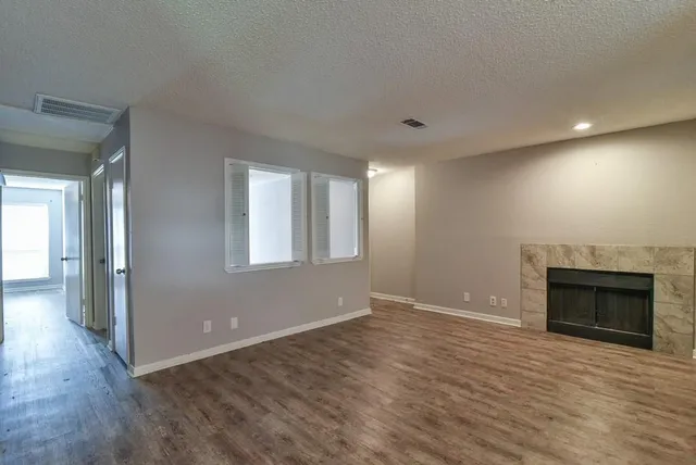 an empty room with wooden floor fireplace and windows