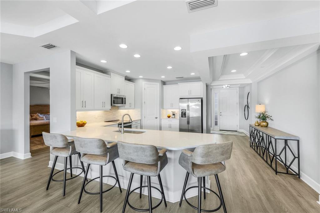 9641 Montelanico Loop, Unit 103 Naples, FL 34119 - Photo 6 of 28 a kitchen with stainless steel appliances kitchen island granite countertop a dining table chairs refrigerator and microwave