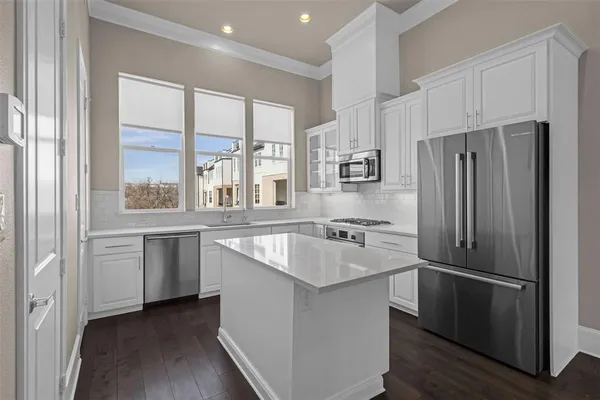 a kitchen with stainless steel appliances granite countertop a refrigerator a sink and white cabinets with wooden floor