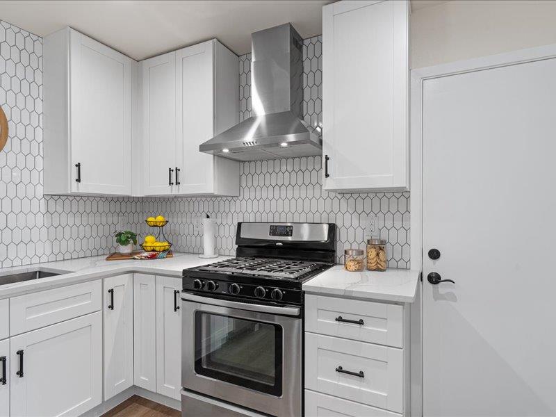 1312 Hyman Lane Austin, TX 78742 - Photo 12 of 36 The kitchen features white cabinetry with black hardware, a stainless steel range with an overhead exhaust hood, and a white geometric tile backsplash