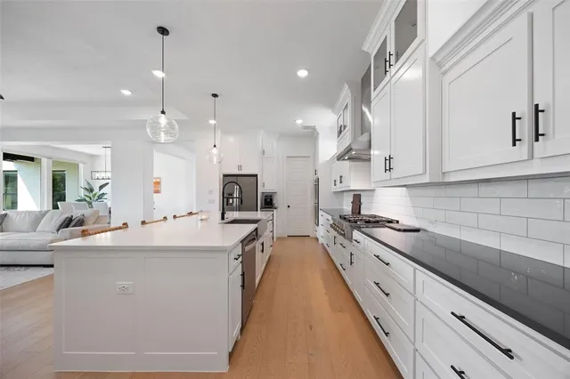 a large kitchen with kitchen island a stove a sink a refrigerator and white cabinets with wooden floor