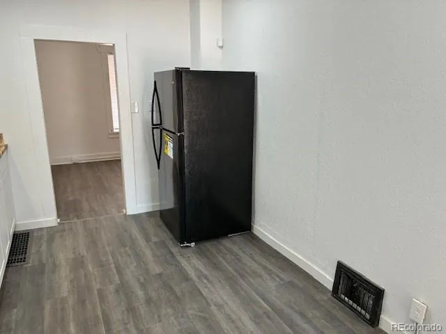 a view of a refrigerator in kitchen and an empty room with wooden floor