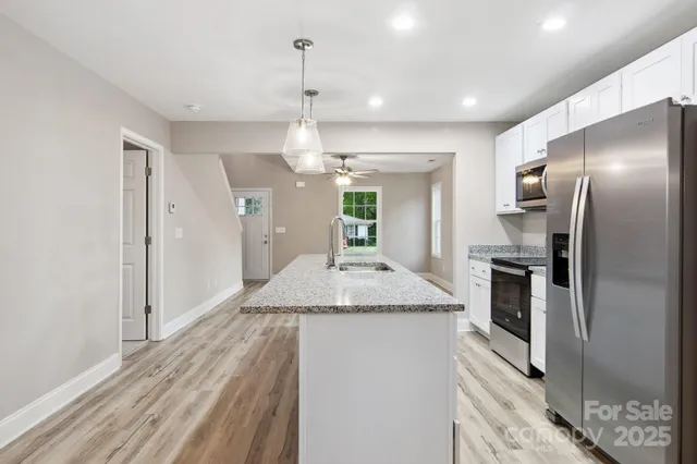 a kitchen with stainless steel appliances granite countertop a refrigerator a oven and white cabinets with wooden floor