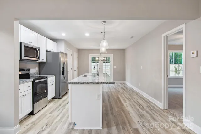 a kitchen with stainless steel appliances granite countertop a refrigerator a stove oven a sink dishwasher and a refrigerator with wooden floor