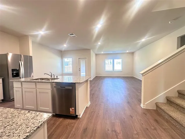 a kitchen with stainless steel appliances granite countertop a refrigerator a sink dishwasher a stove and white countertops with wooden floor