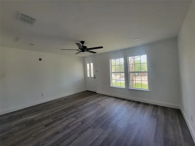 an empty room with wooden floor fan and windows