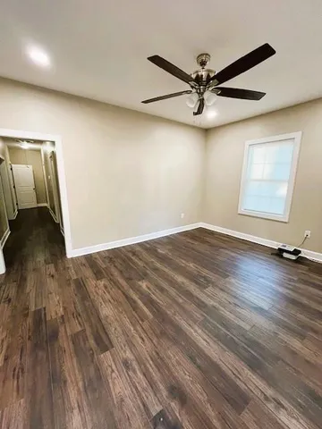 an empty room with wooden floor fan and windows