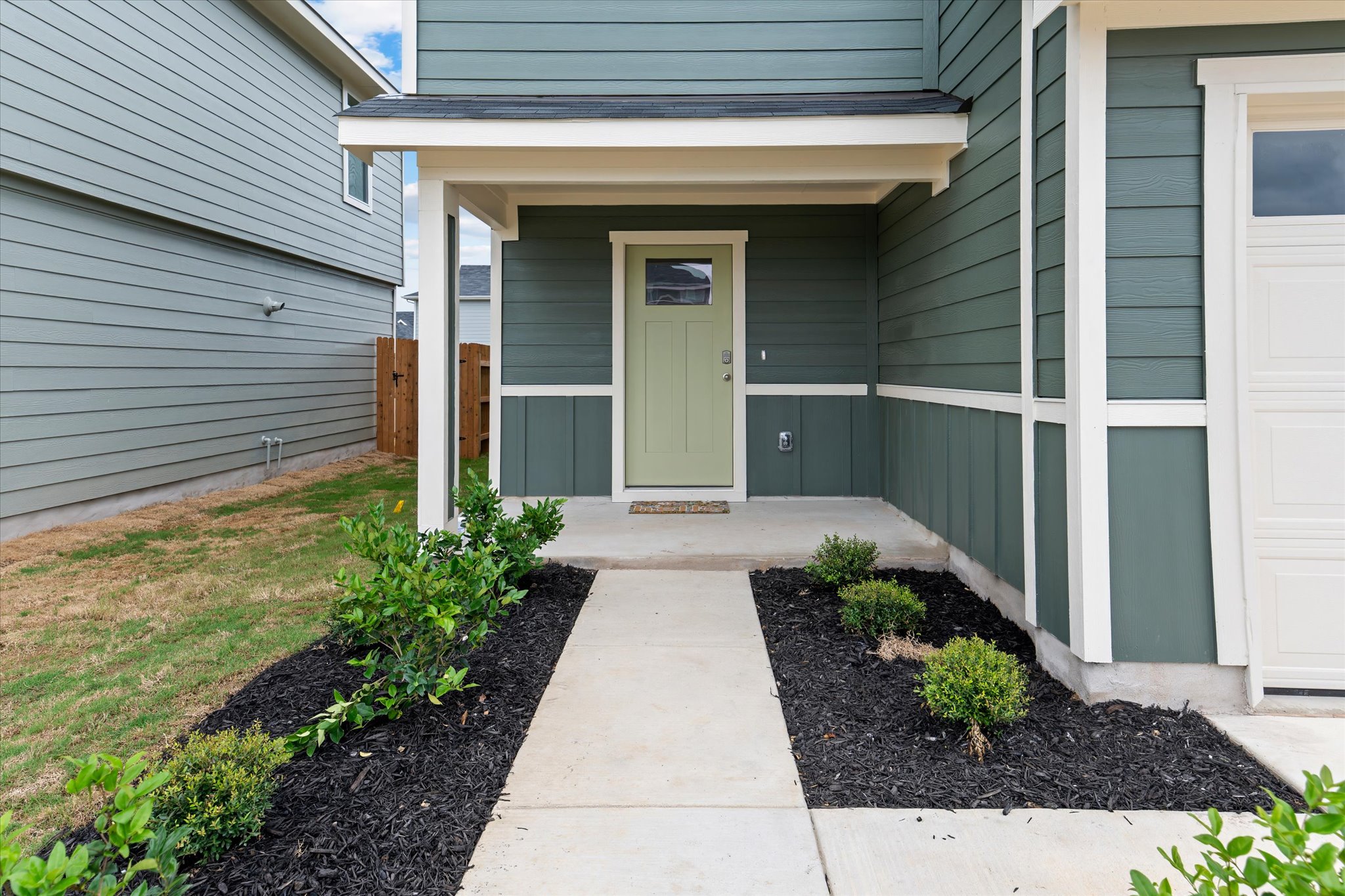 456 Sandringham Loop Kyle, TX 78640 - Photo 4 of 40 A welcoming concrete path leads to a covered entry with a light green front door, complementing the home's deep green siding.
